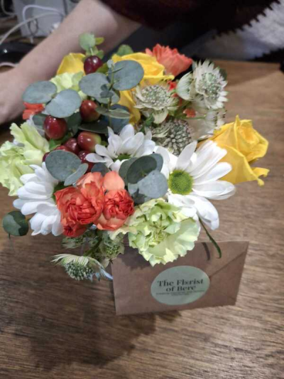 Sunshine Garden - A cheerful and compact arrangement bursting with warm golden tones, soft whites, and lively coral accents. Nestled in a rustic-style container, this design combines fresh greenery, textured elements, and playful pops of color for a bright, uplifting feel. The natural, slightly wild styling gives it a fresh-from-the-garden charm, making it perfect for small gifts, thank-you gestures, or adding a touch of happiness to any space.